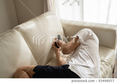 A man lying on the sofa and playing with his smartphone 83498057