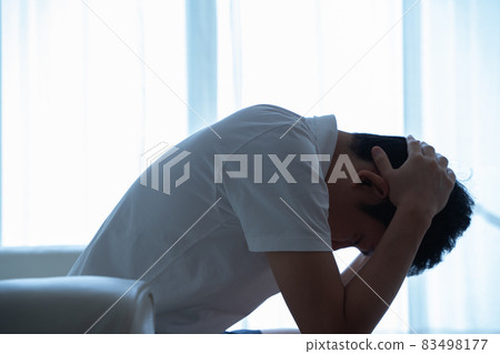 一個人坐在沙發上，抱著頭 83498177