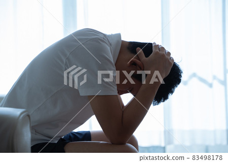 A man sitting on the sofa and holding his head A man sitting on the sofa and holding his head 83498178