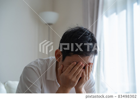A man sitting on the sofa holding his face with his hands A man sitting on the sofa holding his face with his hands 83498302