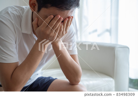 A man sitting on the sofa holding his face with his hands 83498309