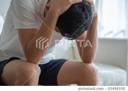 A man sitting on the sofa and holding his head 83498350