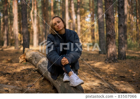 Girl sitting on a log in a pine forest in autumn. Girl sitting on a log in a pine forest in autumn. 83507066