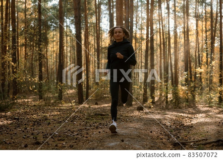 Young athletic woman jogging in forest in sunny morning. Healthy lifestyle concept Young athletic woman jogging in forest in sunny morning. Healthy lifestyle concept 83507072