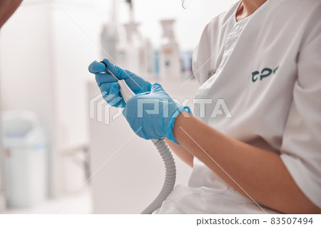 Perdicure master polishes toenail of client with grinding tool at procedure in salon 83507494