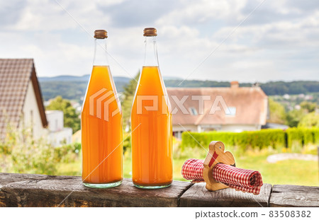 Two bottles of natural apple juice on the background of an Alsatian landscape Two bottles of natural apple juice on the background of an Alsatian landscape 83508382
