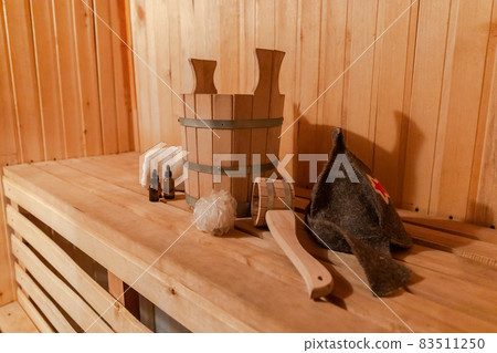 Traditional old Russian bathhouse SPA Concept. Interior details Finnish sauna steam room with traditional sauna accessories set basin towel aroma oil scoop felt. Relax country village bath concept. 83511250