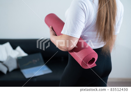 Young chubby woman folds sports mat after online fitness class Young chubby woman folds sports mat after online fitness class 83512430