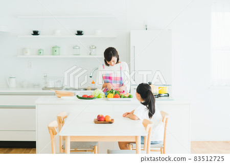 Young mother cooking in the kitchen and elementary school girl in the dining room 83512725