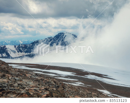 Storm on the top of a mountain. Wonderful dramatic landscape with big snowy mountain peaks above low clouds. Atmospheric large snow mountain tops in cloudy sky. Storm on the top of a mountain. Wonderful dramatic landscape with big snowy mountain peaks above low clouds. Atmospheric large snow mountain tops in cloudy sky. 83513123