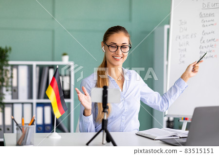 Online languages school. Friendly female tutor giving German lesson, using smartphone, explaining grammar Online languages school. Friendly female tutor giving German lesson, using smartphone, explaining grammar 83515151