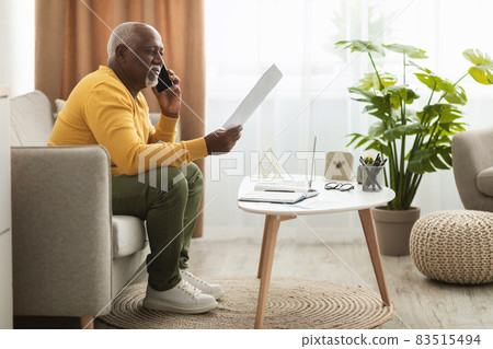 Senior African Businessman Talking On Phone Holding Paper Indoors, Side-View 83515494