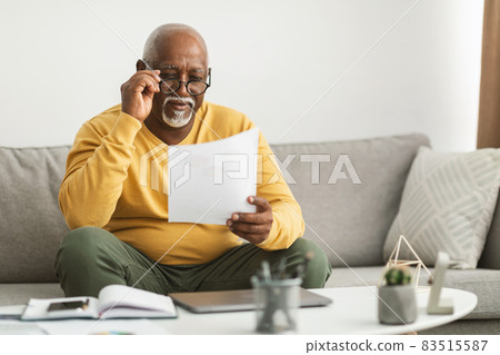 Senior African Male Working With Papers Wearing Eyeglasses Sitting Indoor Senior African Male Working With Papers Wearing Eyeglasses Sitting Indoor 83515587