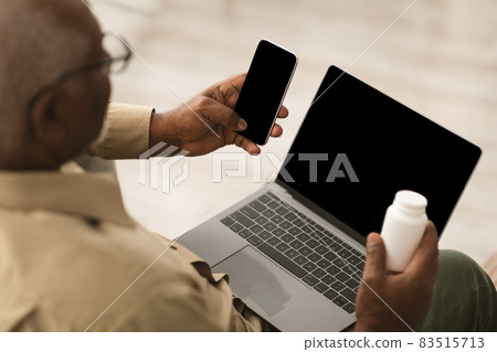 Senior African Man Using Phone And Laptop Holding Medication Indoors 83515713