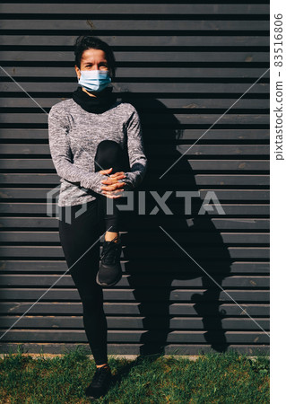 Happy young woman in medical mask stretching legs outdoors 83516806