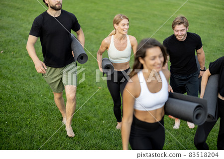 People walking with fitness mats on green meadow 83518204