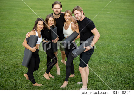 People with fitness mats standind in green meadow People with fitness mats standind in green meadow 83518205