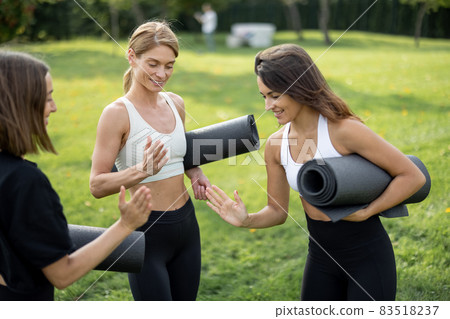 Girls with fitness mats bumping fists on meadow Girls with fitness mats bumping fists on meadow 83518237