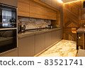 Interior details. Kitchen in a modern apartment. Natural materials. Household appliances, kettle, coffee machine, built-in oven, microwave. Bar counter, high chair. Designer wood panel on the wall 83521741
