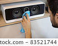 An unrecognizable Caucasian man does a wet cleaning, dusting a musical speaker system. Spring cleaning concept, hygiene in the house, changing roles in the family. Soft selective focus 83521744