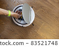 Unrecognizable man cleans a robot vacuum cleaner. Takes out or inserts the dust container. Top view, place for text. The concept of home spring cleaning, helping men to women in the household 83521748