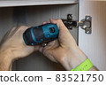 An unrecognizable man installs a door on a wardrobe, fixes furniture with a screwdriver. Only hands are visible. Close-up. Renovation concept, furniture assembly, service sector. Side view 83521750