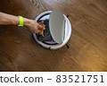 Unrecognizable man cleans a robot vacuum cleaner. Takes out or inserts the dust container. Top view, place for text. The concept of home spring cleaning, helping men to women in the household 83521751