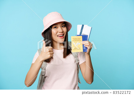 Smiling happy asian tourist, girl shows thumbs up and international vaccination certificate, vaccine passport and tickets, standing over blue background Smiling happy asian tourist, girl shows thumbs up and international vaccination certificate, vaccine passport and tickets, standing over blue background 83522172