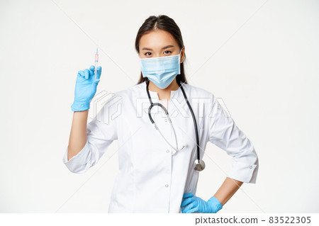 Asian nurse in medical mask holding syringe with vaccine, concept of healthcare and vaccination, standing in clinic uniform, white background 83522305