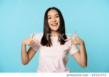 Confident korean woman smiling, makes smug face and points at herself, self-promoting, volunteering, being a winner, standing over blue background Confident korean woman smiling, makes smug face and points at herself, self-promoting, volunteering, being a winner, standing over blue background 83522372