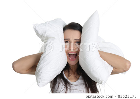 Portrait of young screaming woman covering ears with pillow 83523173