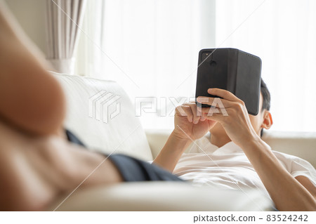 A man lying on the sofa and playing with his smartphone 83524242