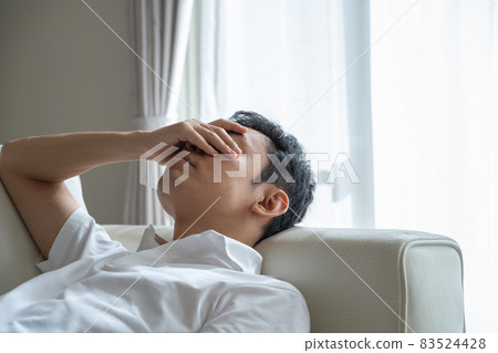 A man lying on the sofa and holding his eyes 83524428