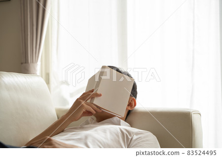 A man lying on the sofa and putting a book on his face A man lying on the sofa and putting a book on his face 83524495