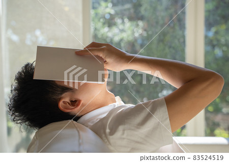 一個男人躺在沙發上，把一本書放在臉上 83524519