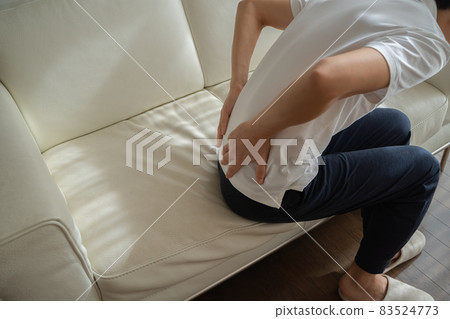 A man sitting on the sofa and putting his hand on his waist 83524773