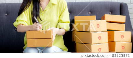 Young asian woman writing address on parcel box at home for delivery order to customer. 83525371