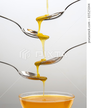 Fresh flower honey drips from a spoon into a spoon on a light background. Organic vitamin food. Fresh flower honey drips from a spoon into a spoon on a light background. Organic vitamin food. 83525844
