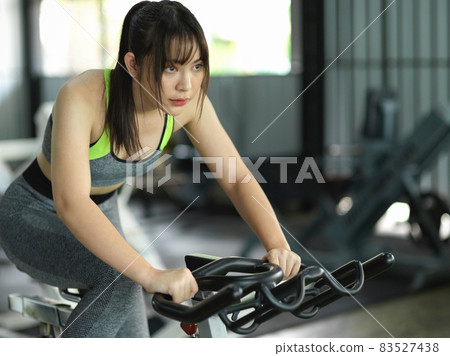 Young strong fitness woman cycling on stationary bike in fitness gym. Young strong fitness woman cycling on stationary bike in fitness gym. 83527438