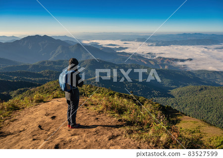 Man hiking looking at mountain range on the top of mountain in tropical forest, Outdoor adventure travel concept Man hiking looking at mountain range on the top of mountain in tropical forest, Outdoor adventure travel concept 83527599