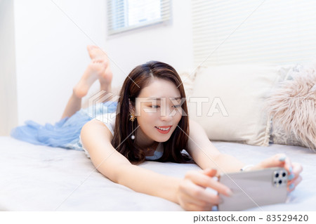 A woman watching a smartphone video while lying face down in bed 83529420