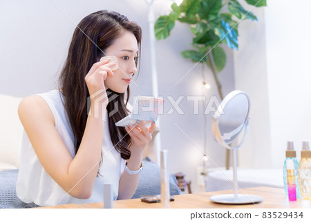A woman looking in the mirror and applying foundation A woman looking in the mirror and applying foundation 83529434