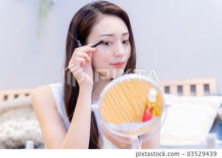 A make-up woman wearing mascara while looking in the mirror 83529439