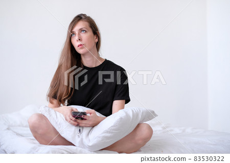 Thoughtful redhead young woman holding mobile phone and thinking in bed. young girl with blue eyes. Sick leave with a phone. Work at home Thoughtful redhead young woman holding mobile phone and thinking in bed. young girl with blue eyes. Sick leave with a phone. Work at home 83530322