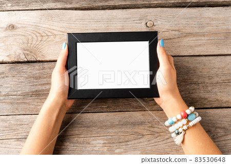 Woman hand holding empty photo frame on wooden table. Top view Woman hand holding empty photo frame on wooden table. Top view 83530648