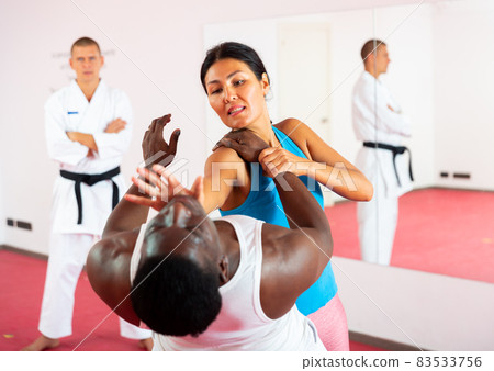 Woman exercising self-defence moves, trainer watching them 83533756