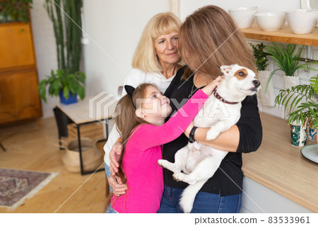 Happy granddaughter and grandmother and daughter having fun with jack russell terrier dog. Grandma hugs grandchild at home. Relationship, family and three generation concept. 83533961