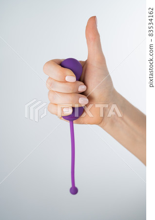 A woman recommends an electronic Kegel trainer for training pelvic floor muscles on a white background. Thumb up 83534162
