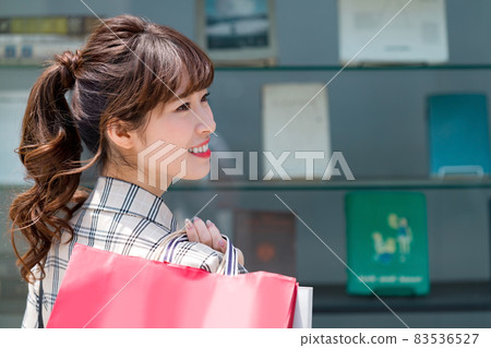 A young woman shopping with a paper bag in front of a shop window 83536527