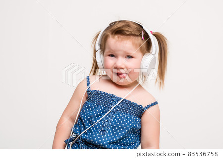 Cute little girl in headphones listening to music using a tablet and smiling on white background 83536758
